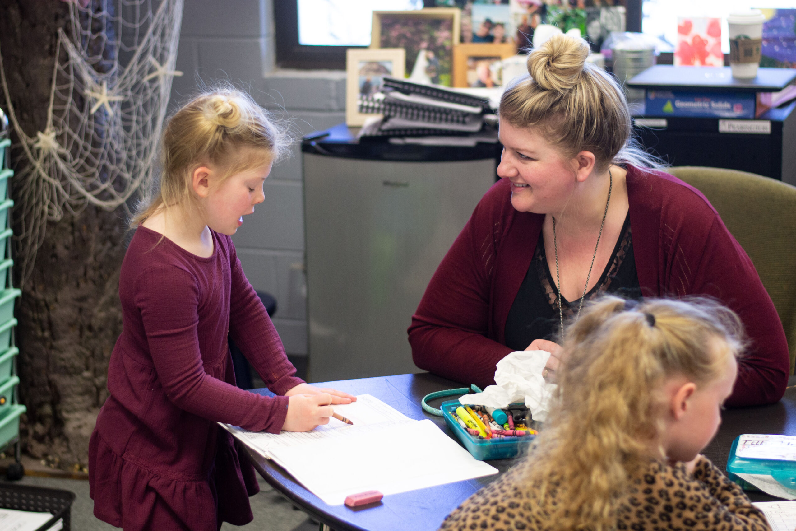 private christian kindergarten student talking to teacher at desk